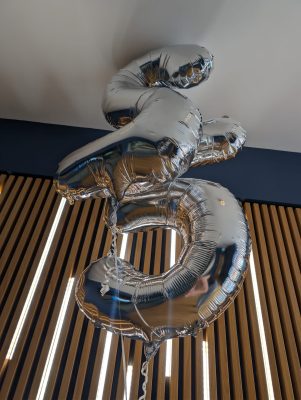 Two silver foil balloons shaped like the number 35 float indoors against a wooden slat wall, symbolising a legacy that will everlast into the future.