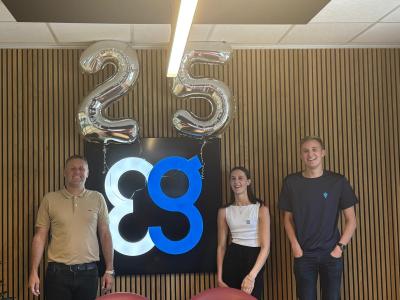 Three people stand in front of a wall with large 25 balloons and a blue and white Everlast logo, celebrating their legacy and looking towards the future.