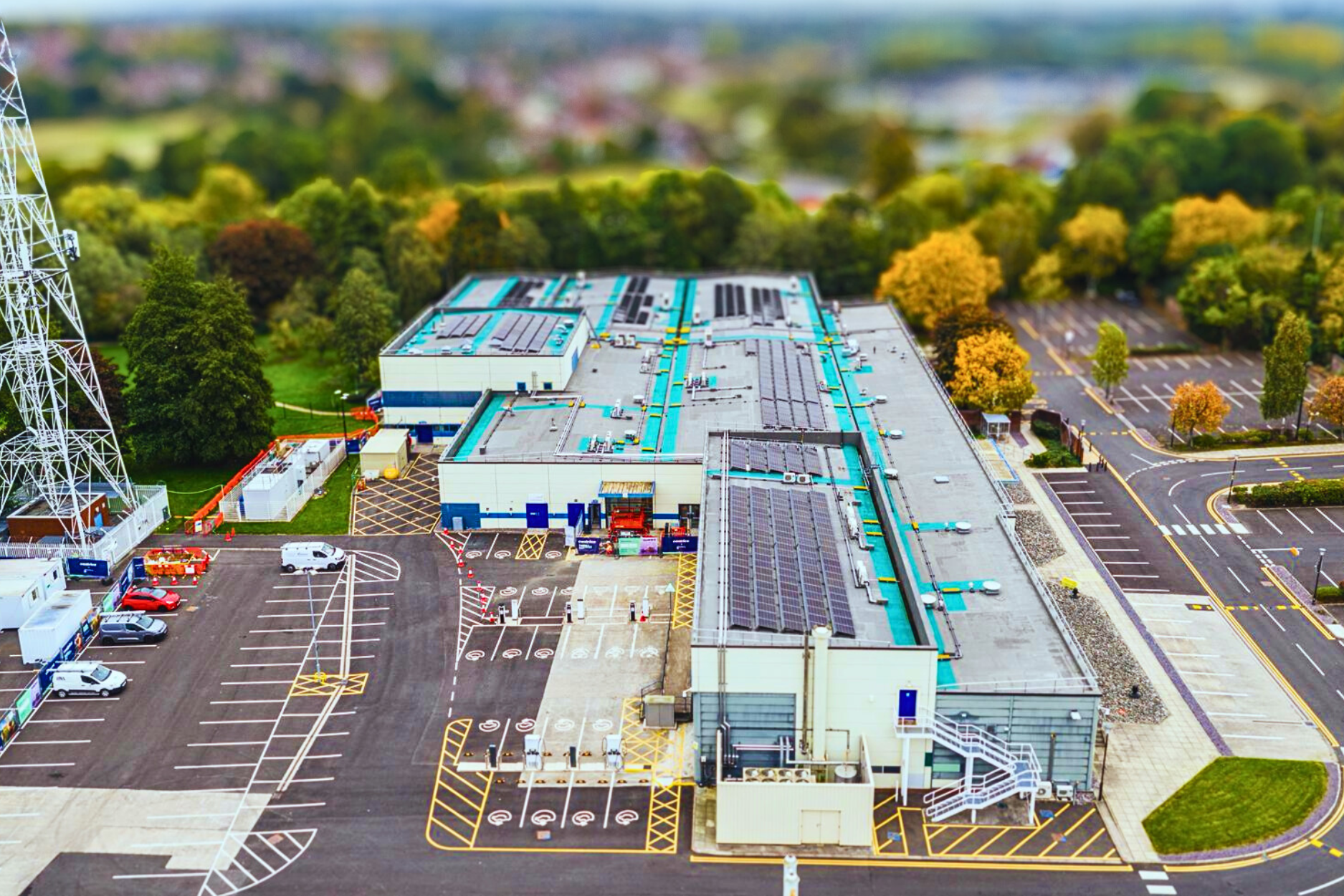 1 Aerial view of a large industrial building with car parks and trees in the background.