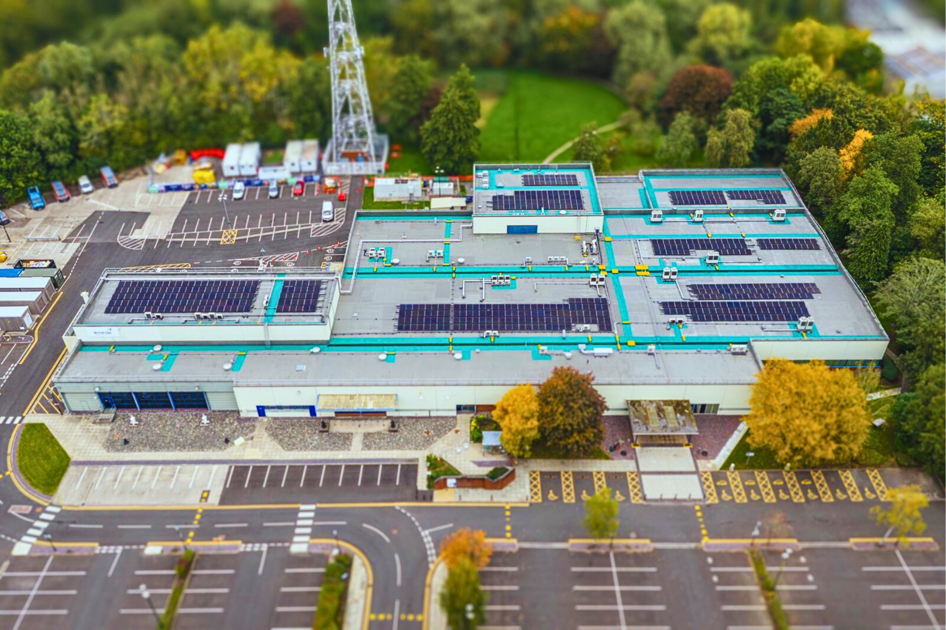 3 Aerial view of a large building with solar panels on the roof, surrounded by trees and parking.