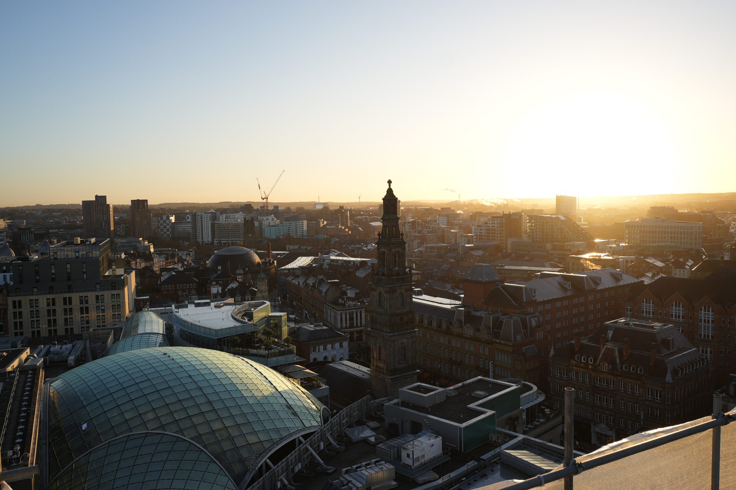 City skyline at sunset with Leeds City Exchange and glass domes by a tall clock tower.