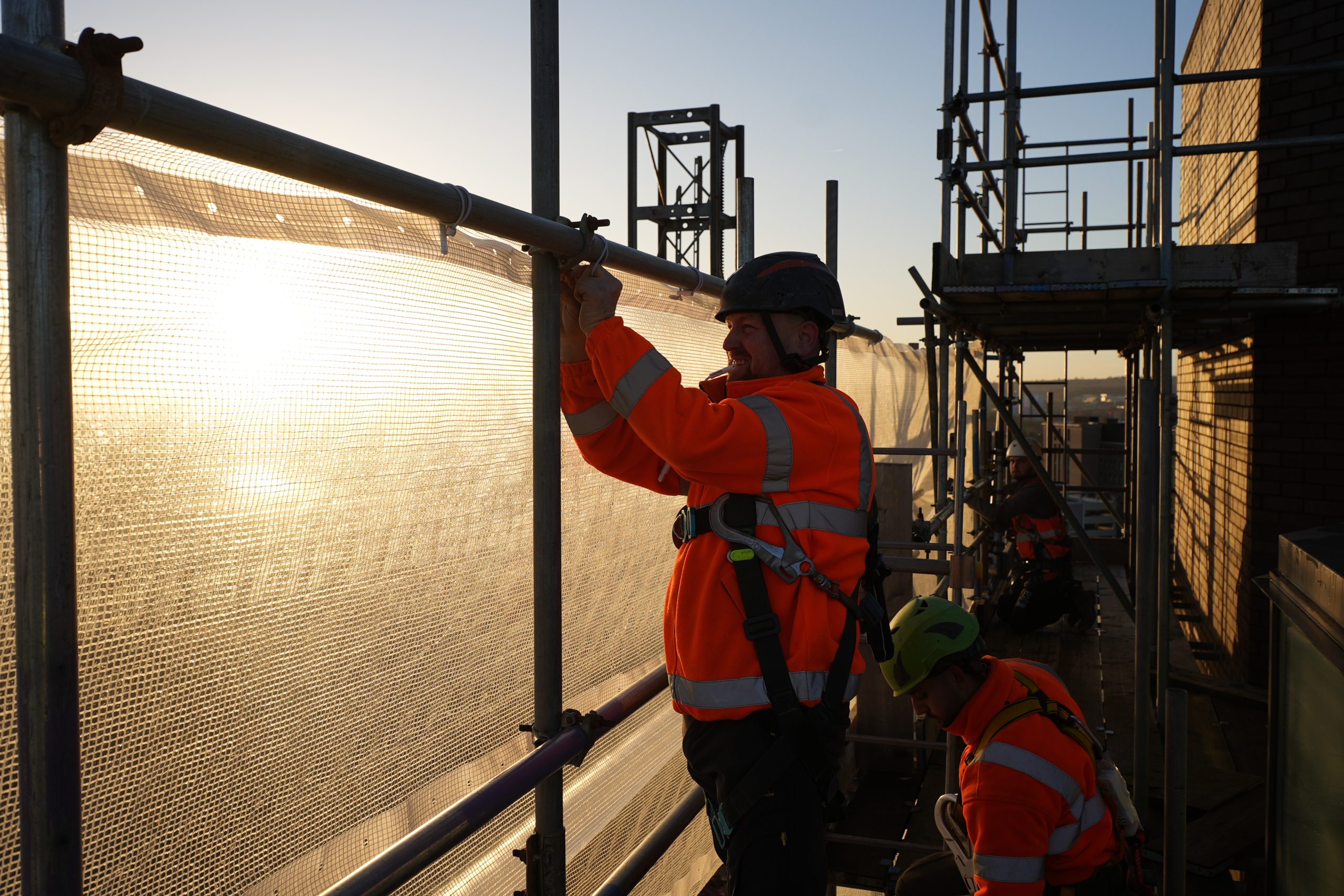 Two construction workers in safety gear work on scaffolding at sunset in Leeds.