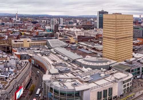 Aerial view of a city with modern buildings and a tall rectangular tower on a cloudy day.