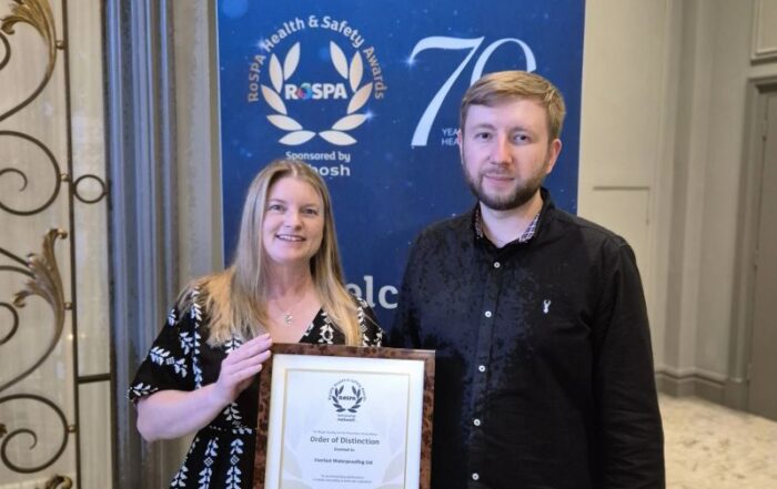 Two people hold a framed certificate at a construction networking Leeds RoSPA display banner.