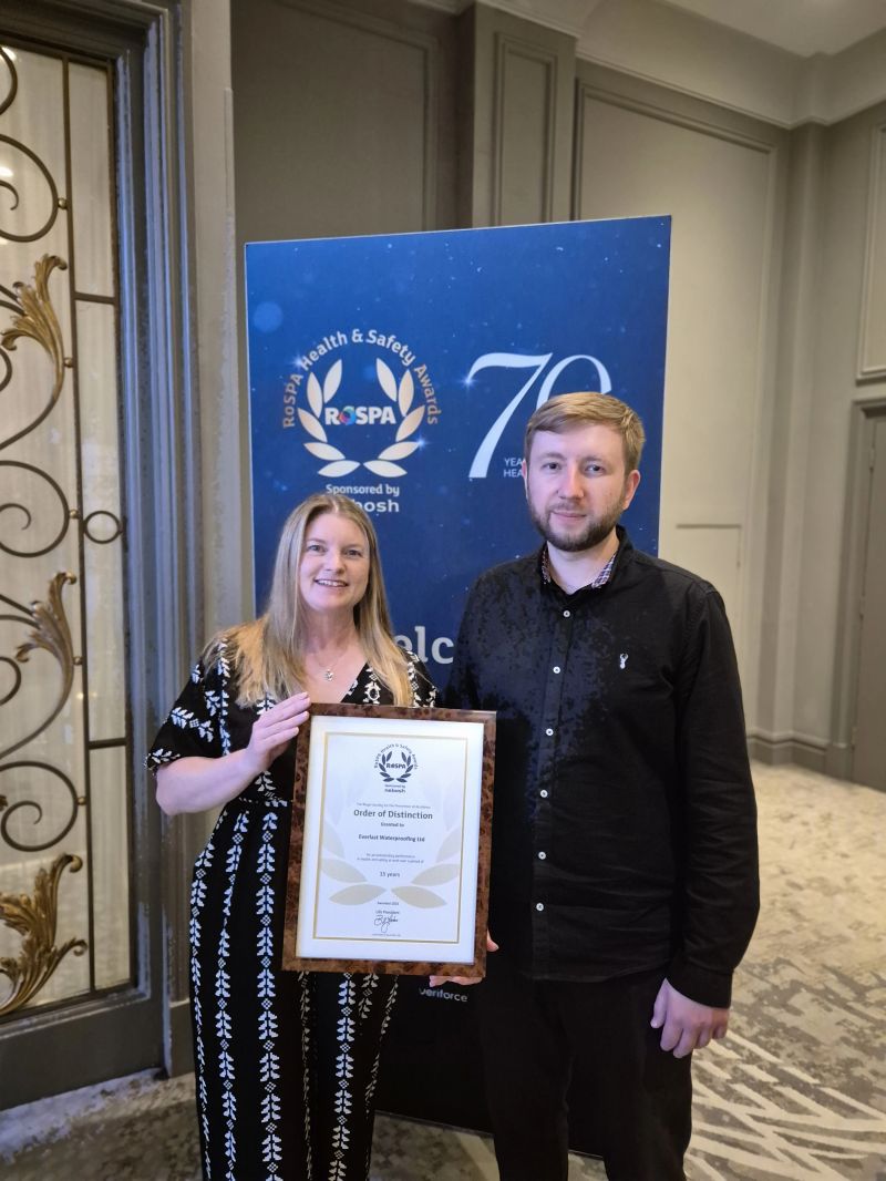 Two people hold a framed certificate at a construction networking Leeds RoSPA display banner.