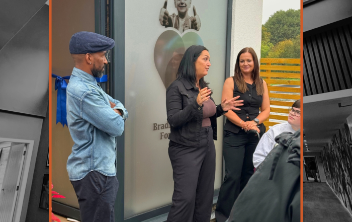A woman at a construction networking event in Leeds speaks to a group by a commemorative window.
